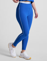 blue high-waisted midi leggings with white contrast piping on side of leg and around waistband.